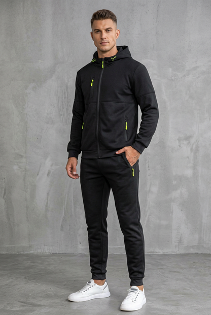 Man in black hooded tracksuit with neon yellow zip pulls, standing against a concrete wall 8