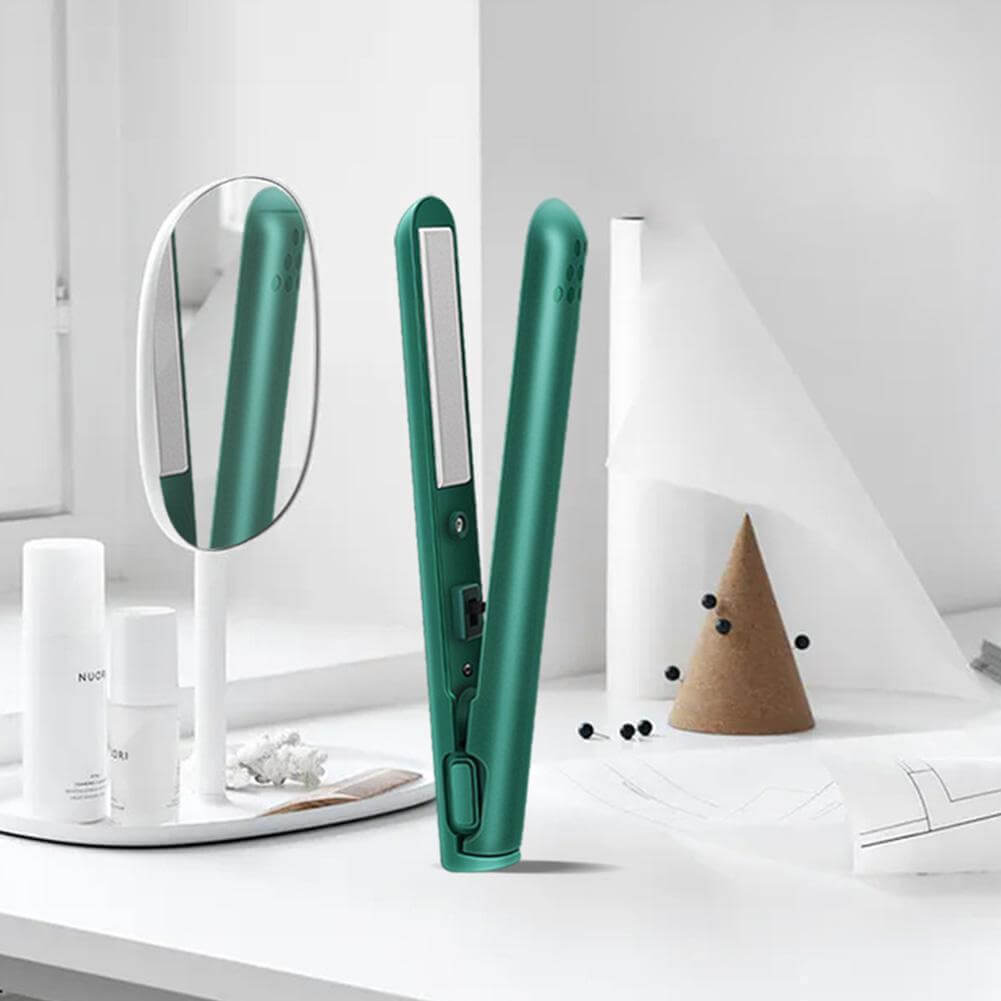 Green straightener standing open on a white dressing table beside a mirror, toiletry bottles and a cork cone ornament. 2