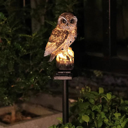Brown owl light lit up at night on its black stake, surrounded by dark foliage and green leaves. 4