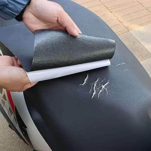 Hands peel the backing from a black patch above scratches on a black scooter seat 3