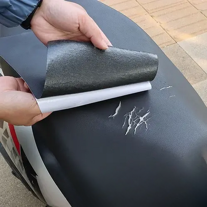 Hands peel the backing from a black patch above scratches on a black scooter seat 3