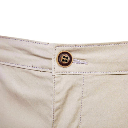 Close-up of the waistband fastening, a brown four-hole button with buttonhole and stitching on beige fabric. 5