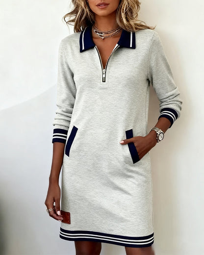 Grey long sleeve dress with half zip and navy trim, model standing with one hand in a side pocket. 3