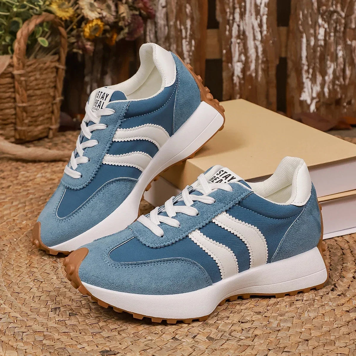 Pair of blue suede and nylon trainers with white stripes, displayed on woven matting beside books 6