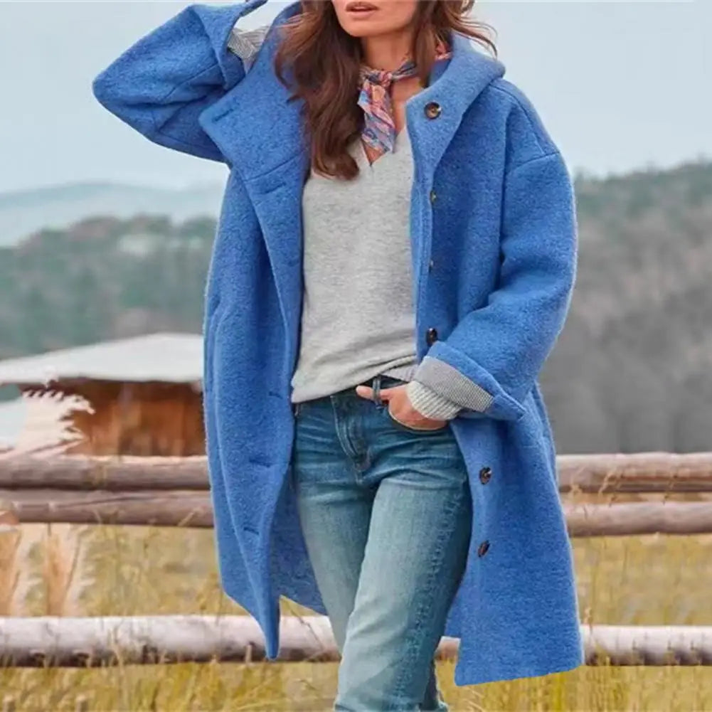 Blue coat worn over a grey top and scarf, one arm raised, standing in front of a wooden fence 6