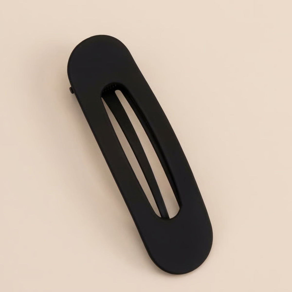 Single matte black slim flat clip with an open slot, lying diagonally on a beige background 5
