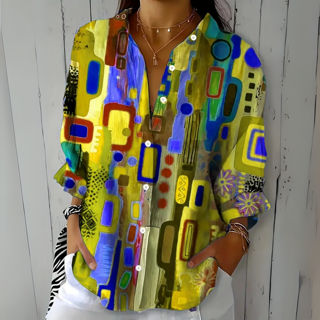 Model wearing the blouse in a yellow colourway with blue and green abstract shapes and a floral cuff detail. 5