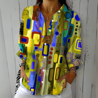 Model wearing the blouse in a yellow colourway with blue and green abstract shapes and a floral cuff detail. 5