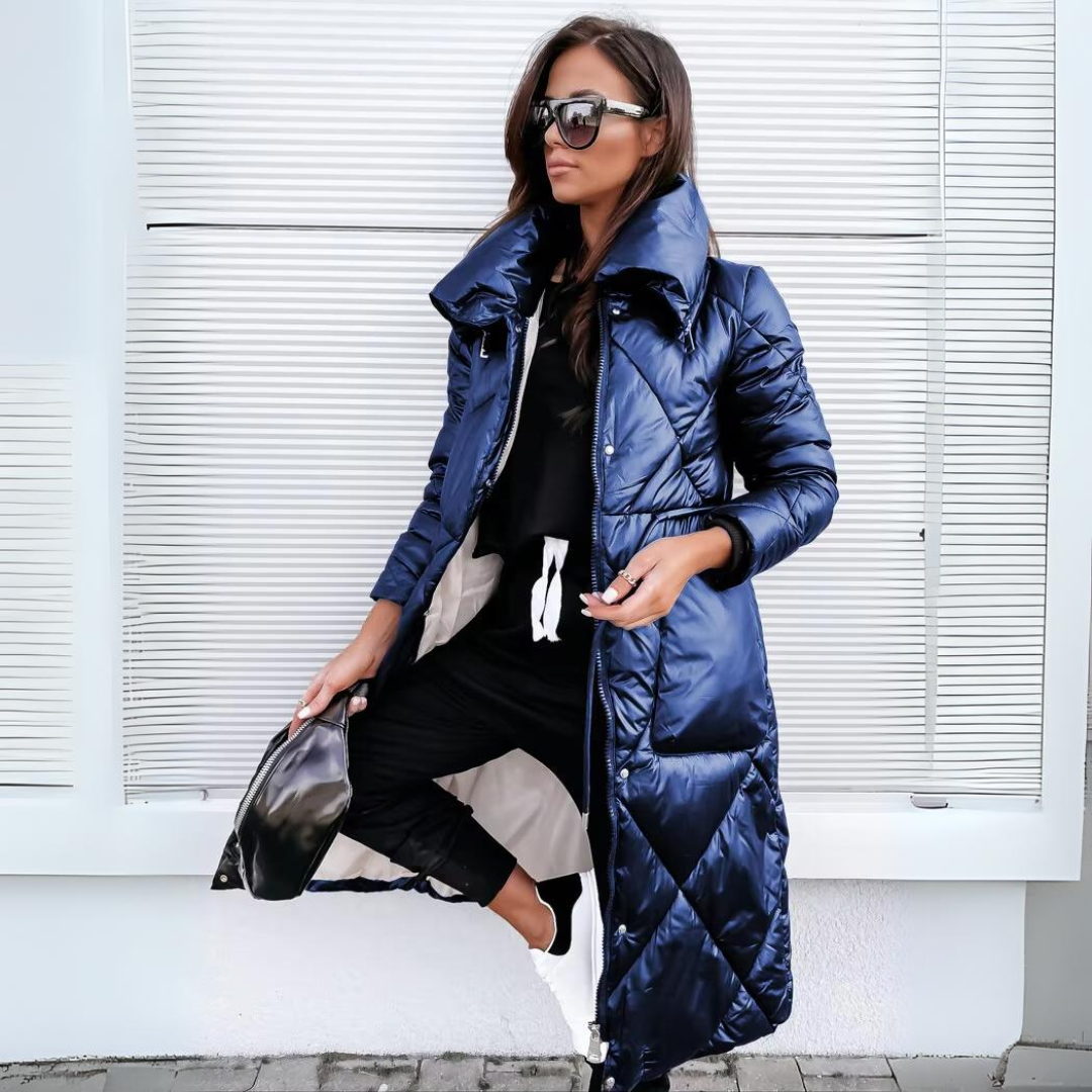 Long diamond-quilted puffer coat in glossy navy blue, worn open over black joggers by a woman holding a black bag. 3