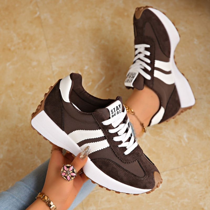 Dark brown trainers with white stripes and chunky white platform soles, held in a hand over a marble floor 3