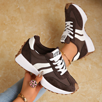 Dark brown trainers with white stripes and chunky white platform soles, held in a hand over a marble floor 3