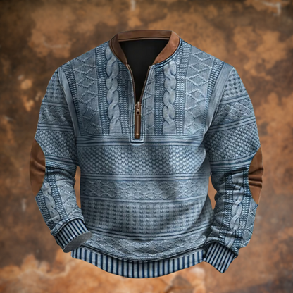 Front view of the blue-grey version with cable and diamond textured panels, brown suede-look collar, zip and elbow patches, against a rusty backdrop. 1