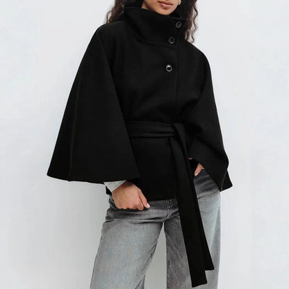 Black cape jacket worn with grey jeans, hands in pockets, belt tied at the front 6