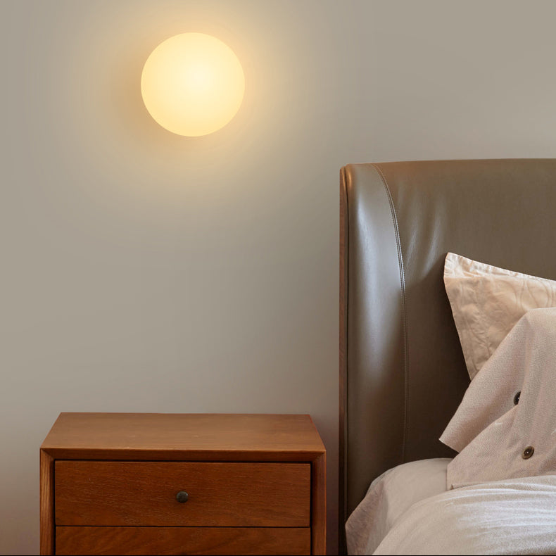 Glowing opal glass sphere mounted on the wall above a wooden bedside cabinet and leather headboard 2
