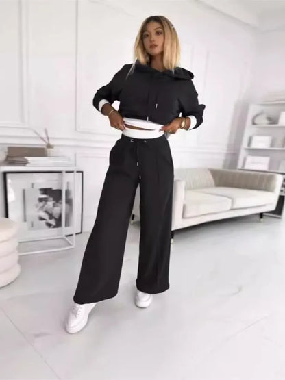 Model in the black cropped hoodie and wide trousers, lifting the hem to show the white layer 6