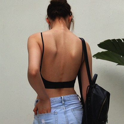 Back view of a model in the black bra with thin straps and a low open back, worn with light denim shorts. 2