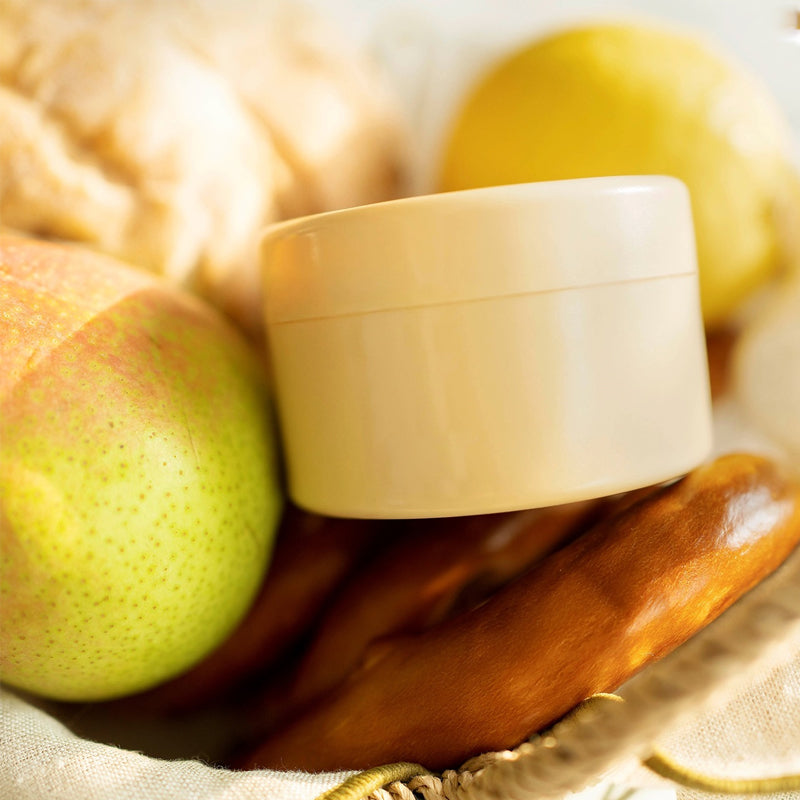 Closed cream round insert nestled between a pear, a lemon and bread in a woven basket. 13