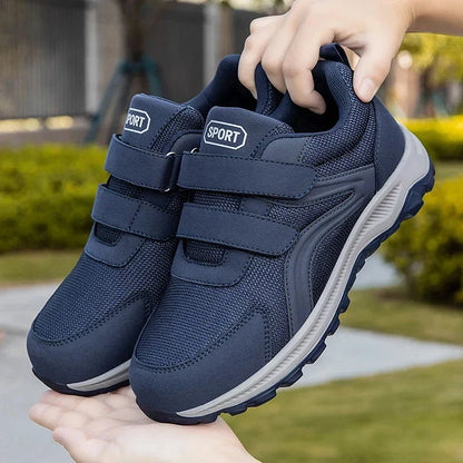 Hand holding up a pair of navy strap shoes against a blurred garden background 12