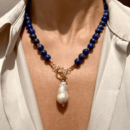 Model wearing the blue bead necklace with its baroque pearl pendant, framed close at the collarbone 4
