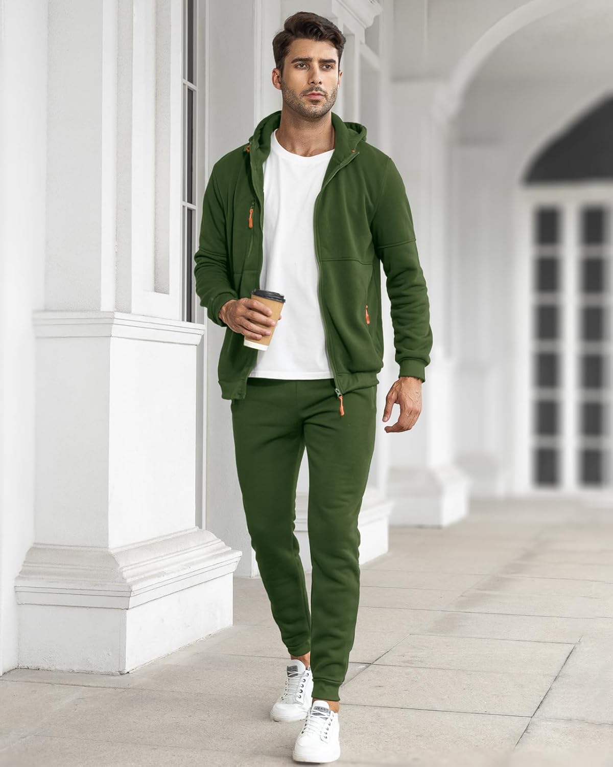 Model walking along a white colonnade in the green tracksuit, jacket open over a white t-shirt 19