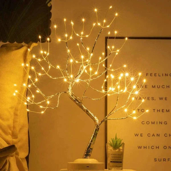 Tree lamp with warm lights on a white base, beside a small succulent and a framed text print 3