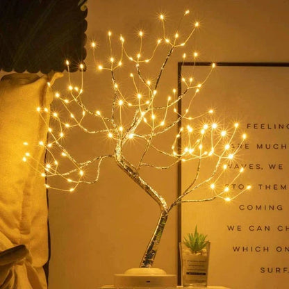 Tree lamp with warm lights on a white base, beside a small succulent and a framed text print 3