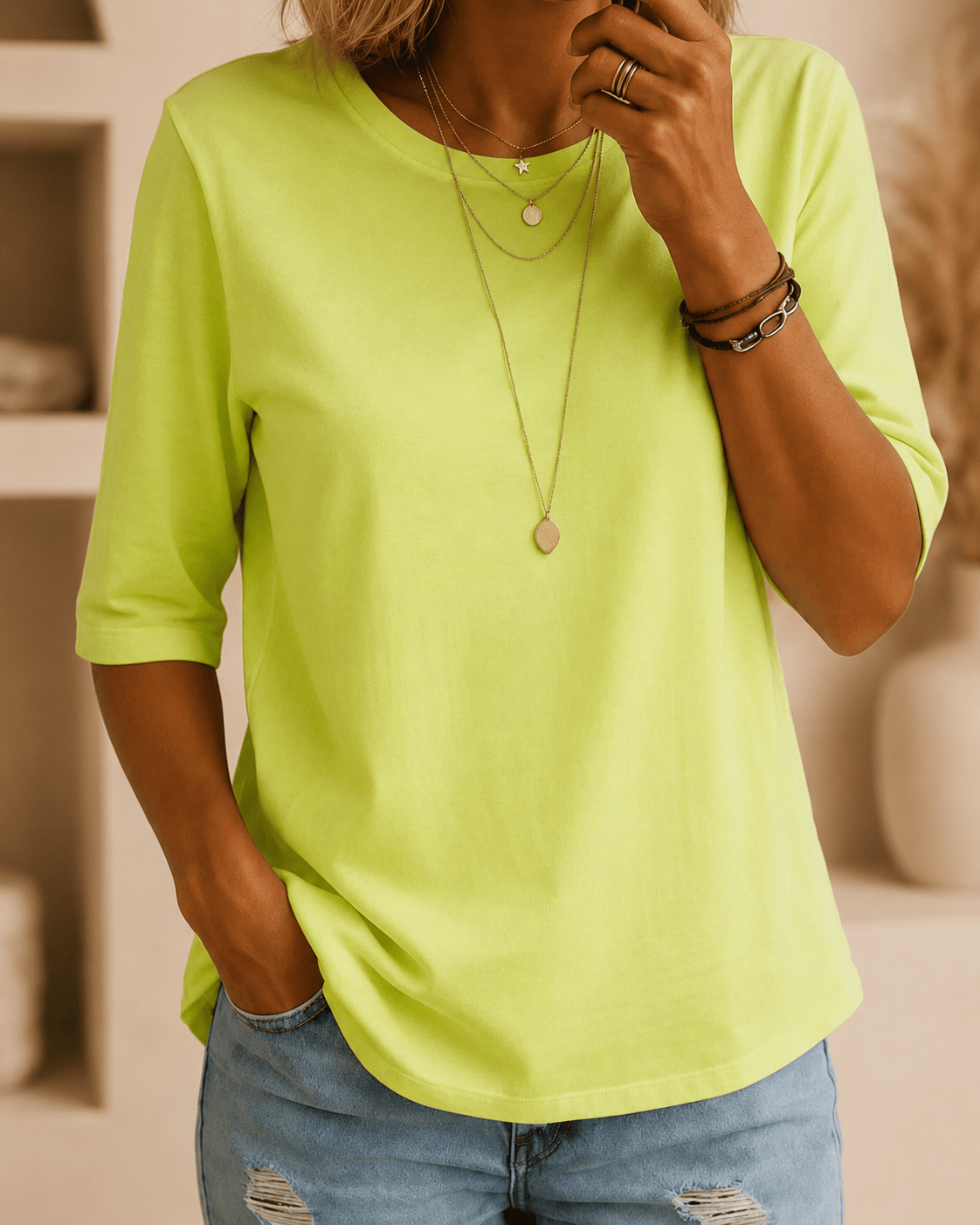 Woman wearing the neon green relaxed-fit tee with light distressed jeans, layered gold necklaces and leather bracelets, one hand in her pocket. 1