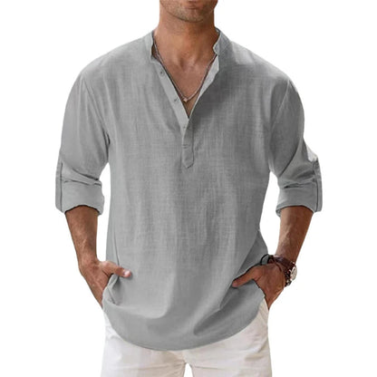 Man wearing the Henley shirt in light grey, with a short button placket, rolled sleeves and hands in white trousers. 6