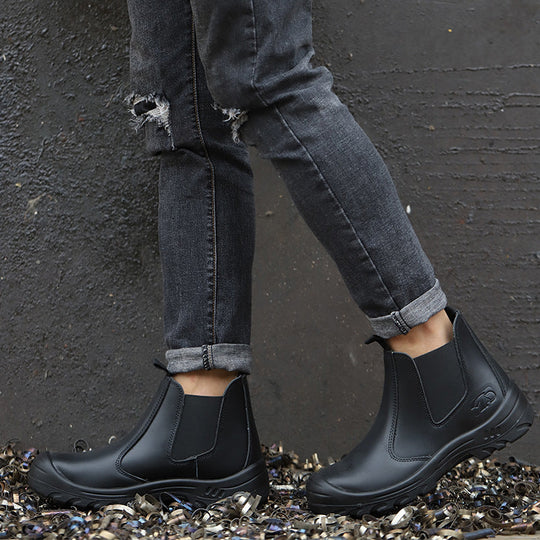 Model in ripped grey jeans wearing black slip-on boots, standing on metal shavings against a dark textured wall 7
