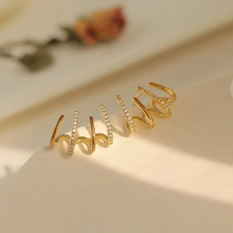 Gold claw earrings with sparkling stones on a cream surface, a dried rose blurred behind 8