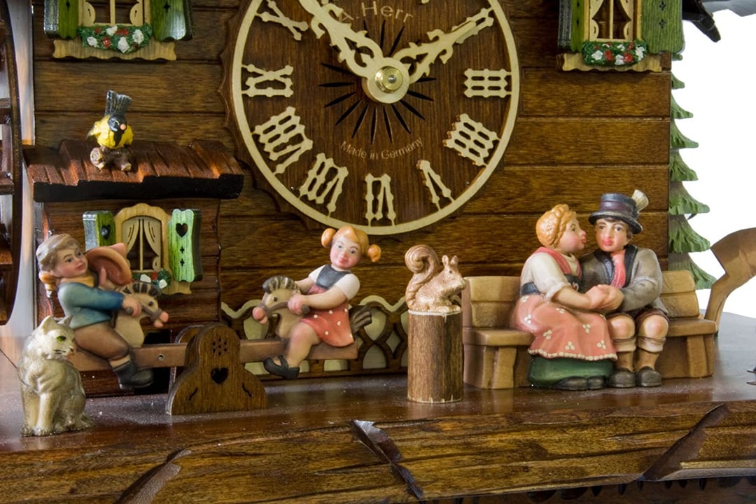 Close-up of the clock base, showing a sweetheart couple on a bench, children on hobby horses, a squirrel, a cat and a small bird. 13