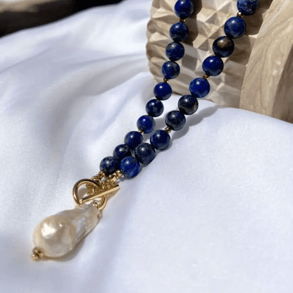Beaded strand and pearl pendant draped over white fabric beside a carved wooden block 6