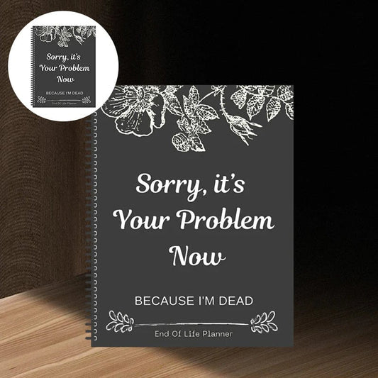 Coil-bound planner with a dark grey cover, white floral line drawings along the top and a bold centred slogan, standing on a wooden shelf. 1