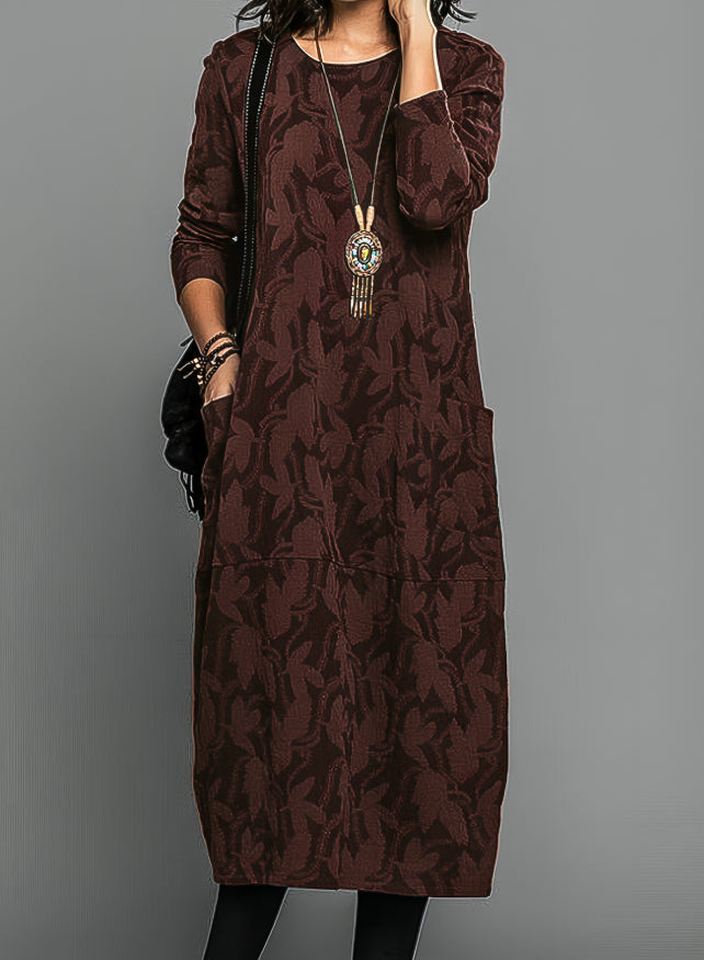 Model wearing the dress in deep burgundy brown with a tonal leaf pattern and a long pendant necklace 2