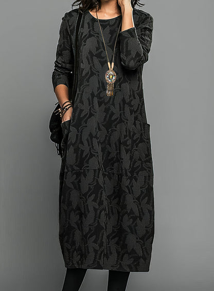 Model wearing the dress in black with a subtle tonal leaf pattern, styled with a tasselled pendant necklace 4