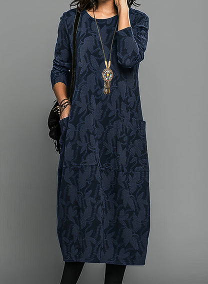 Model wearing the dress in navy blue with a tonal leaf pattern, long sleeves and side pocket 3