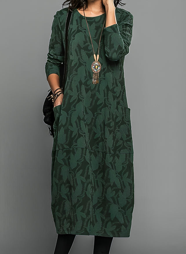 Model wearing the dress in dark green with a tonal leaf pattern, pendant necklace and black tights 1