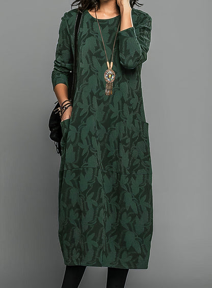 Model wearing the dress in dark green with a tonal leaf pattern, pendant necklace and black tights 1