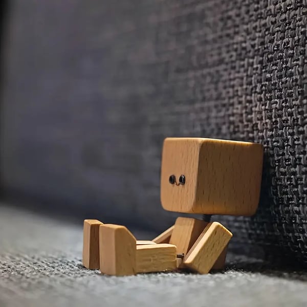 Side view of the wooden figure sitting on grey carpet and leaning against a dark woven fabric surface. 7