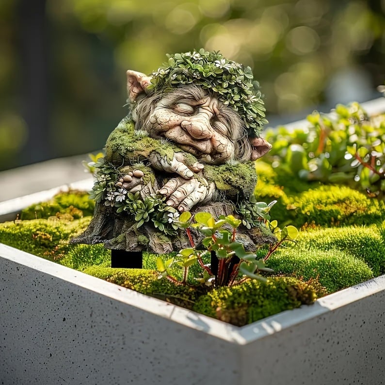 Sleeping troll face with a leafy crown and folded hands on a mossy stump, placed in a planter of moss. 4