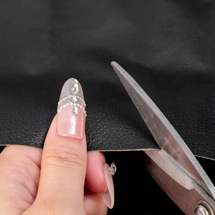 Scissors cut a sheet of black leather-grain material held between a hand's fingers 5