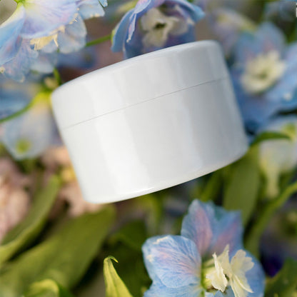 Closed white round insert lying on a bed of blue delphinium flowers and green leaves. 9