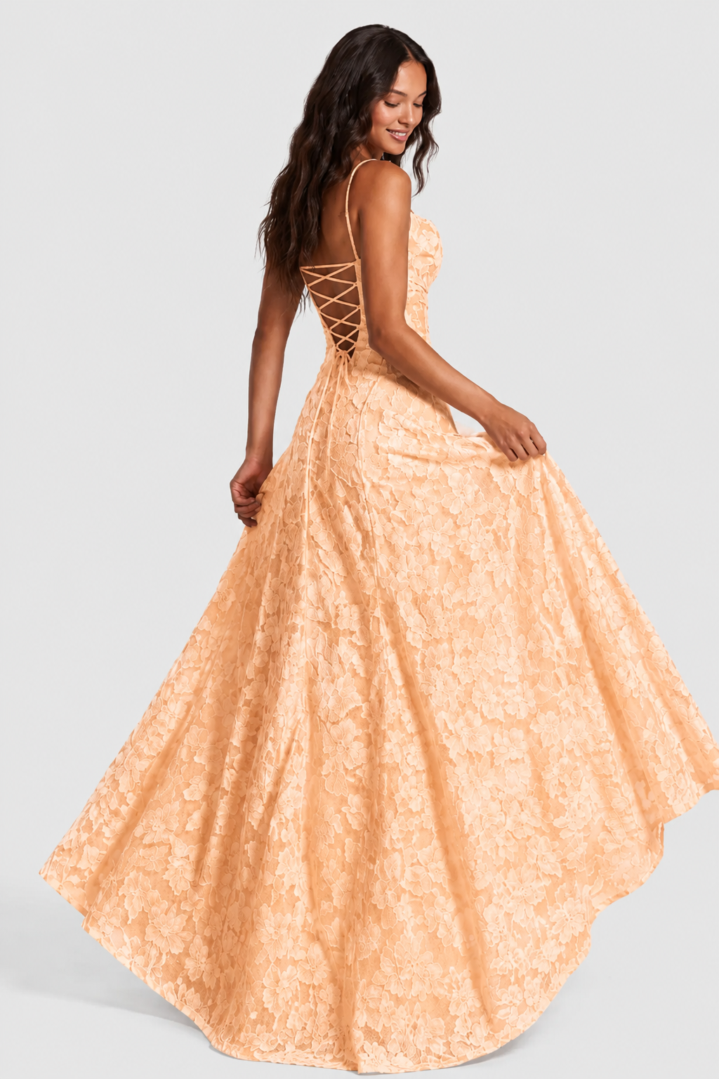 Model in a peach lace gown seen from behind, holding out the skirt to show the lace-up back and fullness. 15