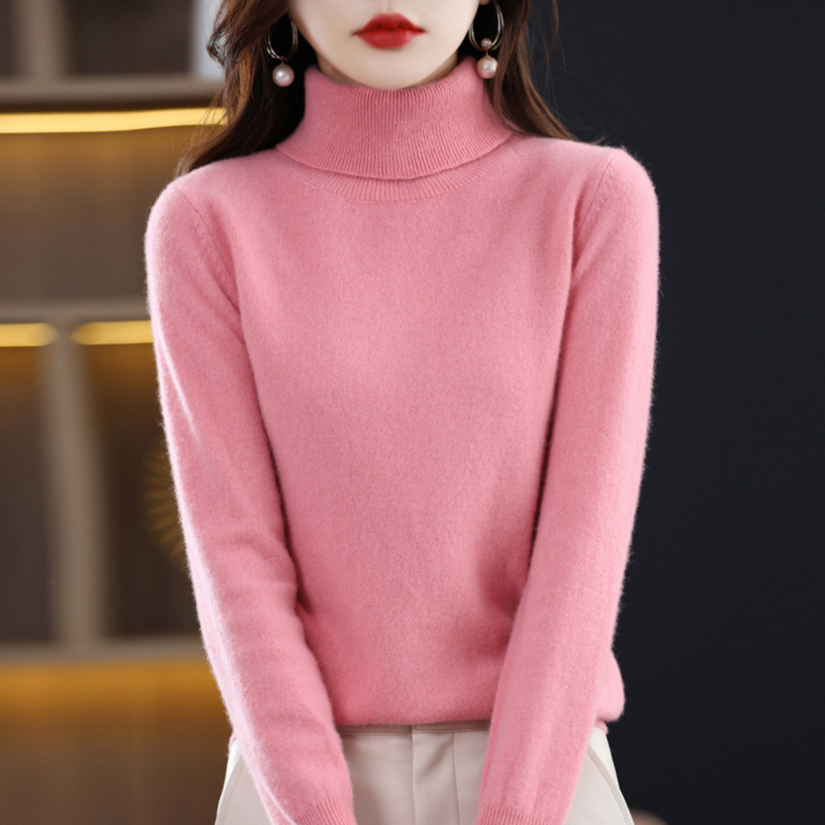 Model standing in a bright pink roll-neck jumper with a ribbed collar and cream trousers, arms relaxed by her sides. 7