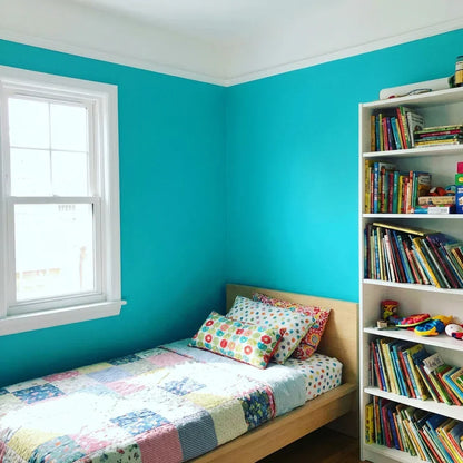 Child's bedroom with turquoise walls, white window trim and ceiling, a patchwork quilt and a full bookcase 9