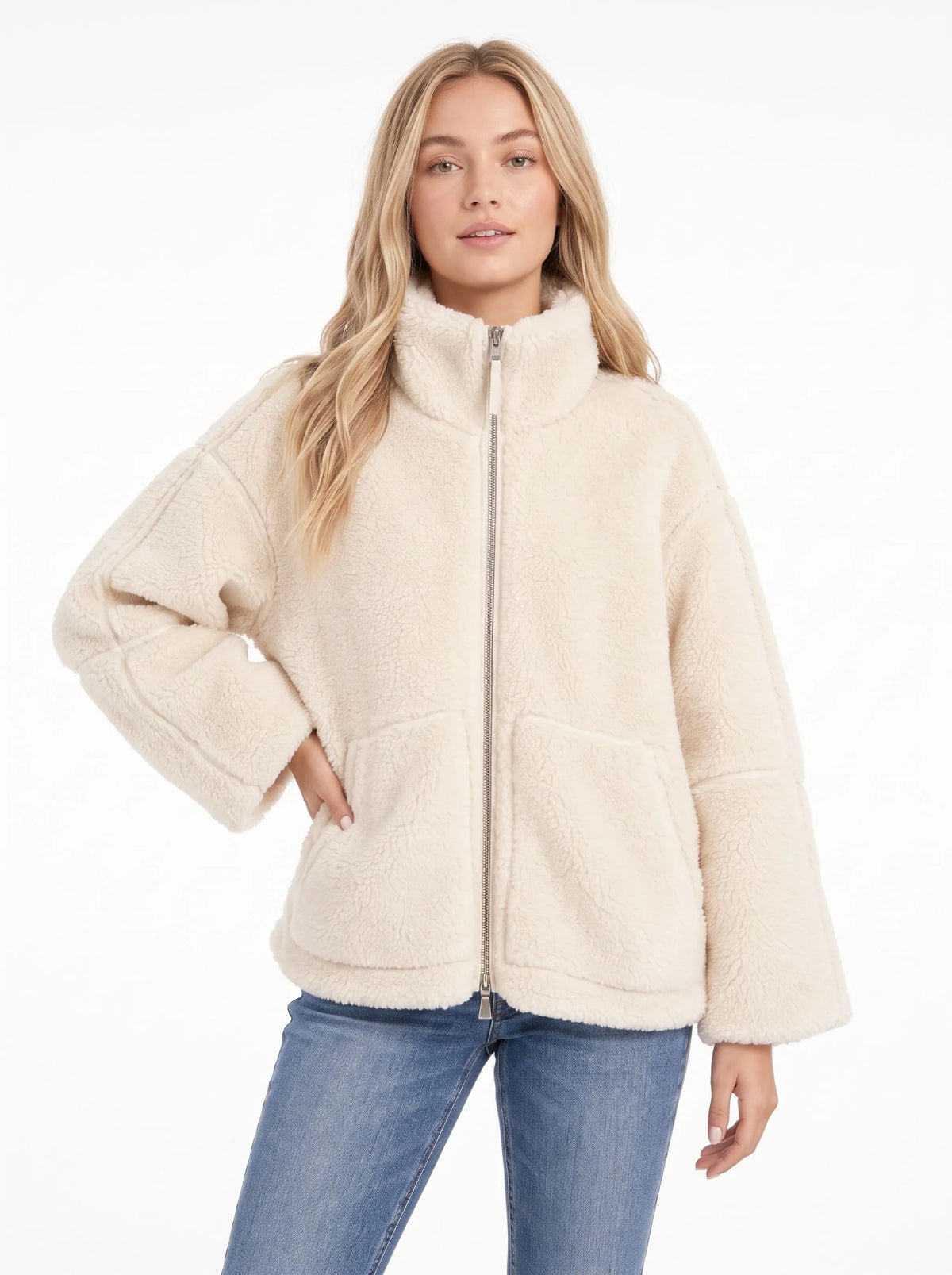 Woman in a cream fleece zip coat with a high collar, one hand on her hip, with blue jeans 8