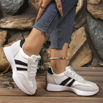 Cream and black striped trainers worn on a model's feet with cropped jeans, in front of a stone wall 5