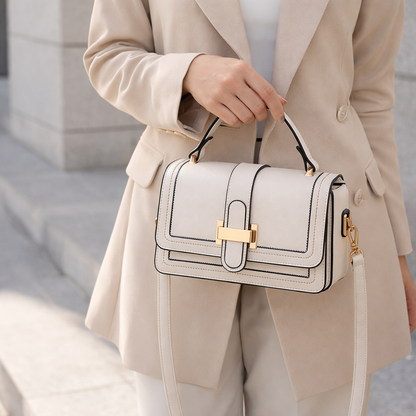 Model in a beige blazer holding the cream bag by its top handle, with the shoulder strap hanging down. 2