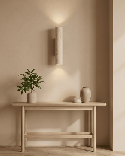 Lit wall light hung above a light wood console table with a plant and ceramic vases 8