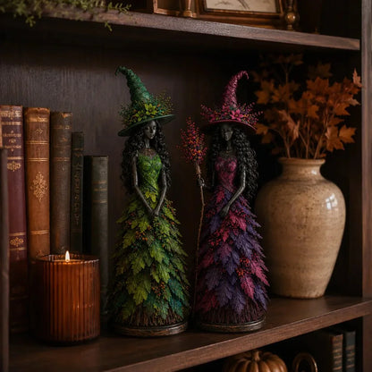 Green and purple witch figurines on a dark wooden bookshelf beside old books, a glowing candle and a vase of dried leaves. 4